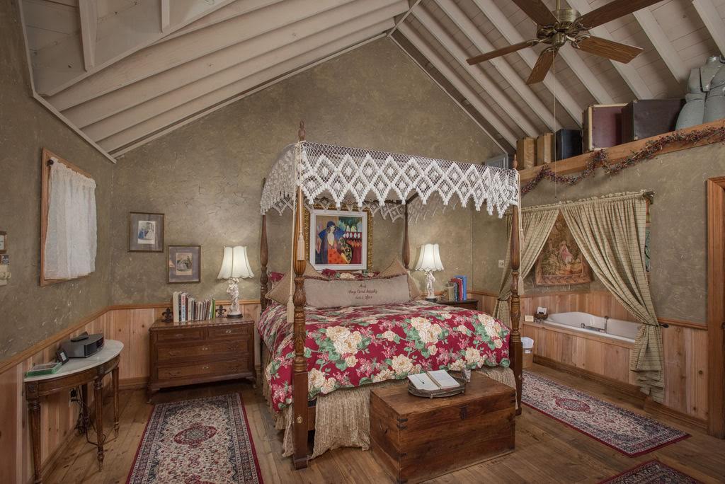 France Cabin littered with French Antiques, a 4 post bed with a floral quilt, and antique luggage shelved over the hot tub in the corner of the room - Texas Bed and Breakfast