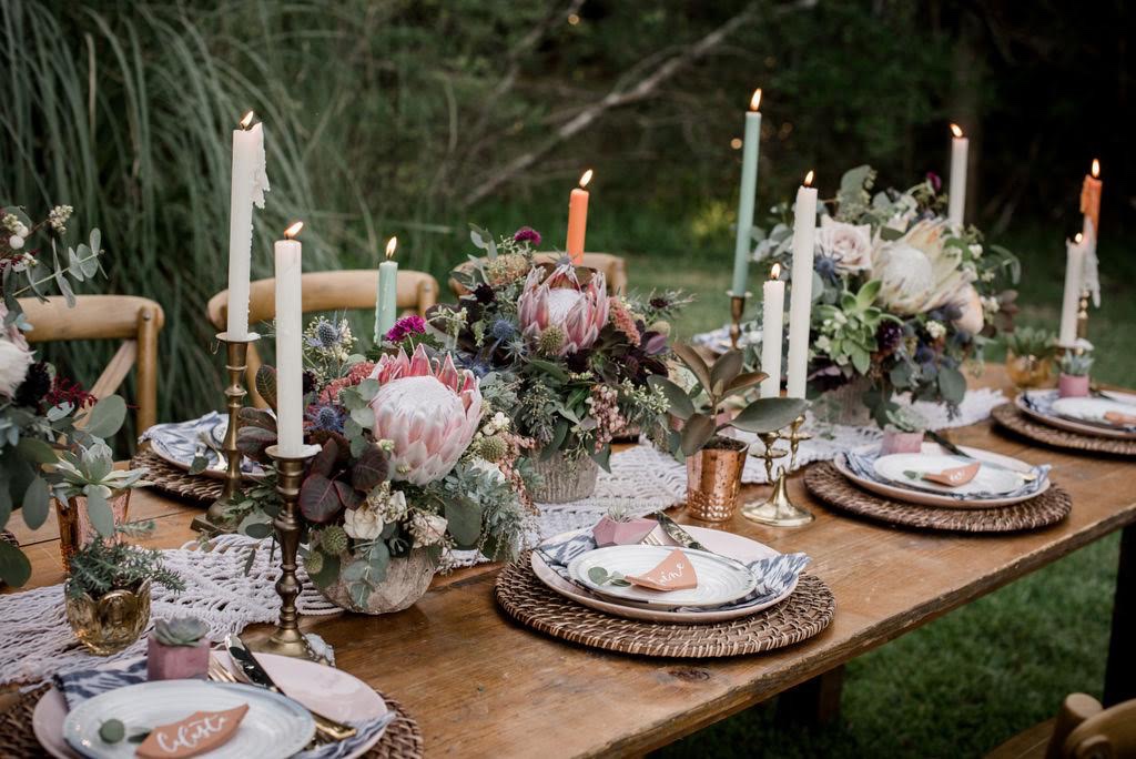 Beautiful Bohemian Tablescape with lighted multi colored candles, succulents, greenery, pottery shard name cards on a plated setup with a wooden oak table - Free Wedding Planning Checklist