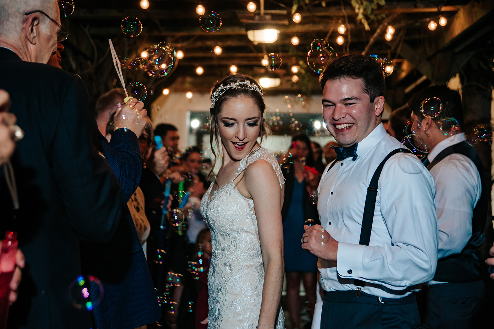 Bride and Groom exiting their wedding reception down a walkway lined with their friends and family while bubbles are blown by guests - Wedding Venue Brochure