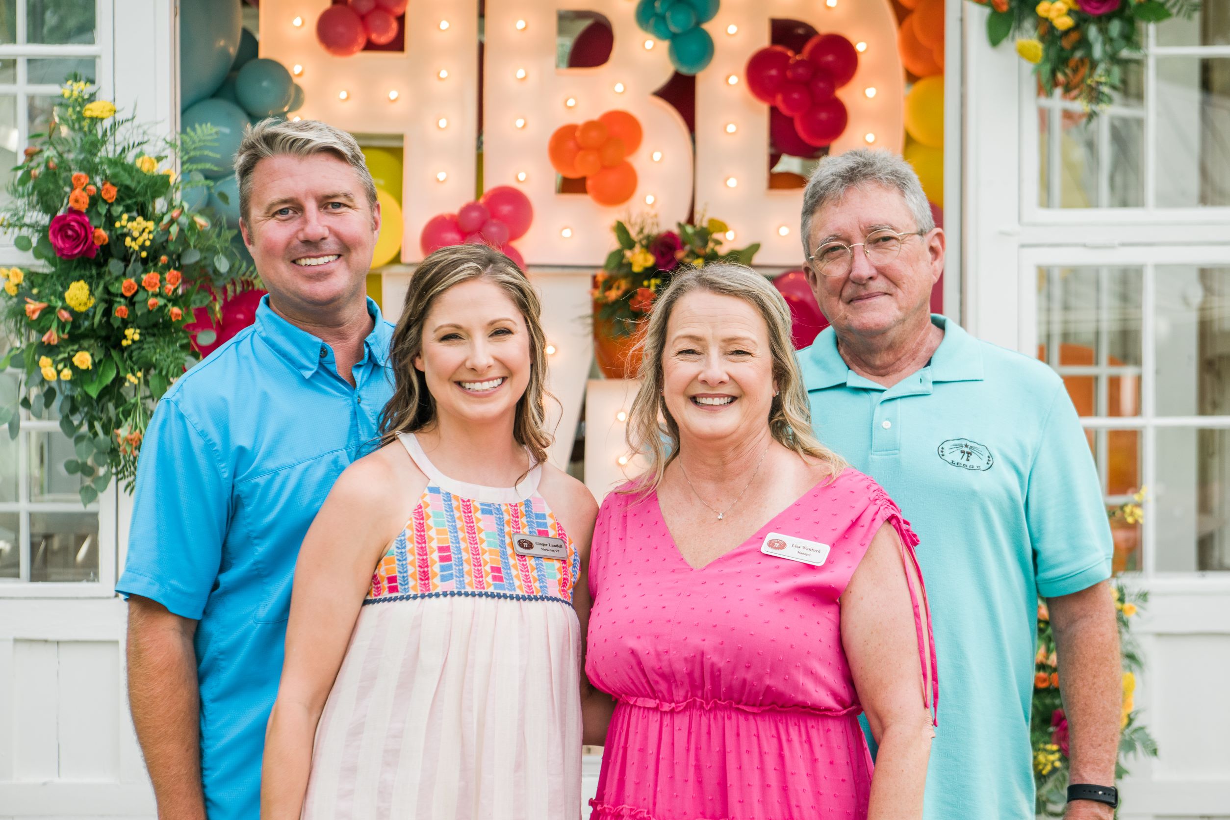The owners of 7F Lodge standing in front of their Chapel for their 25th Anniversary dressed in hues of pastel colors and smiling at the camera - College Station Wedding Venue
