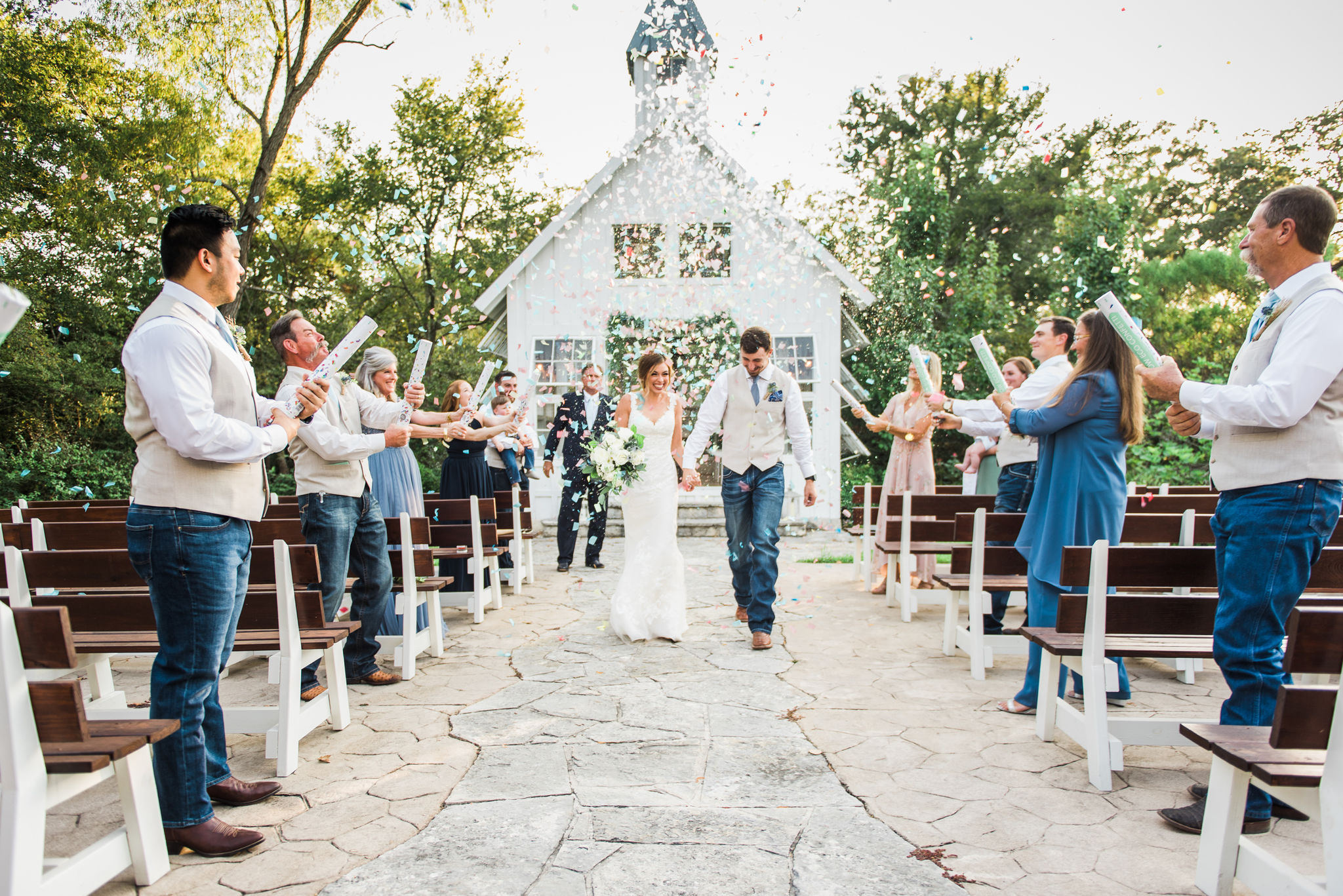 small group of family and friends line the ceremony aisle congratulating the wedding couple walking through multi colored confetti hanging gently in the air after the wedding ceremony - Elopement Package