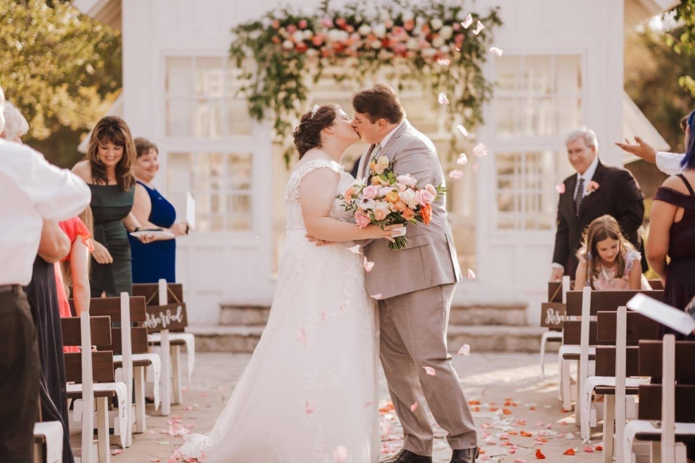 Wedding couple celebrate at the pop of confetti hanging over them and their guests in front of a little white chapel as the bride holds her bouquet like the statue of liberty - Elopement Package