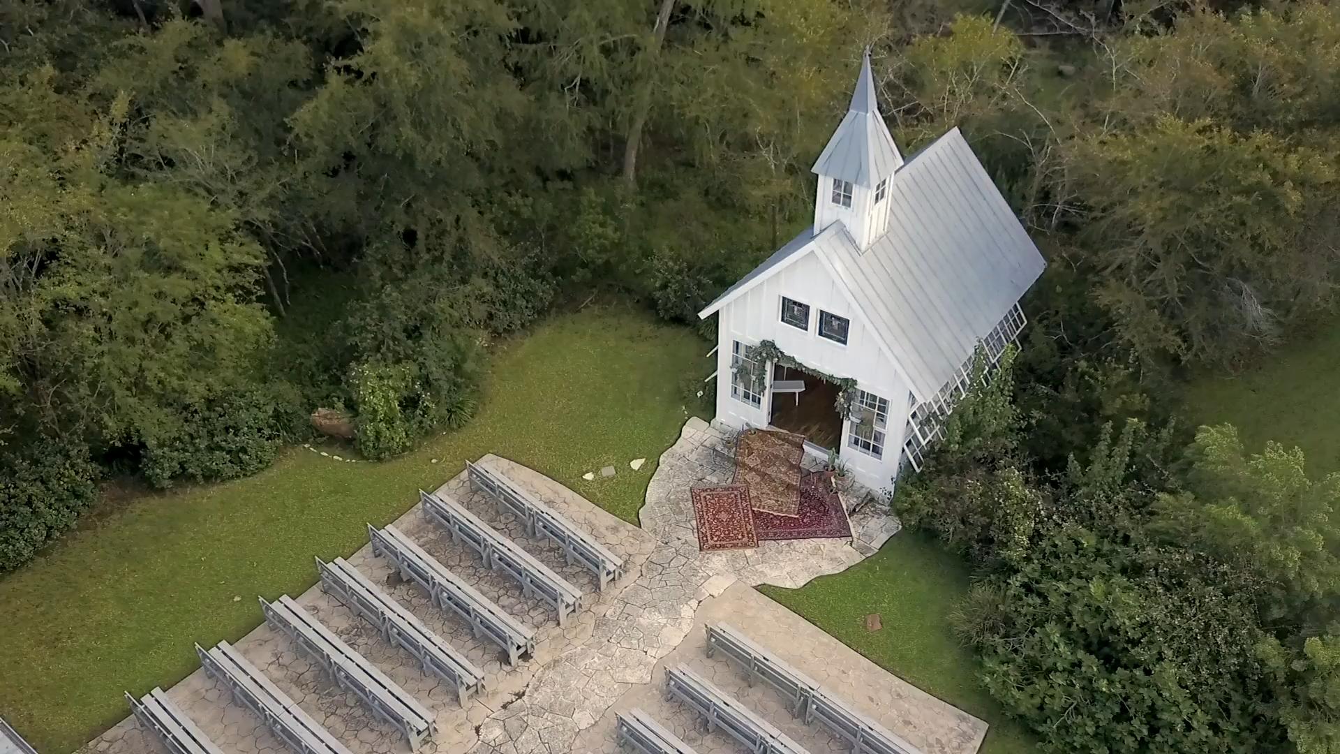 Aerial View of a little white chapel in the woods with lush green trees and grass - Houston Wedding Venue